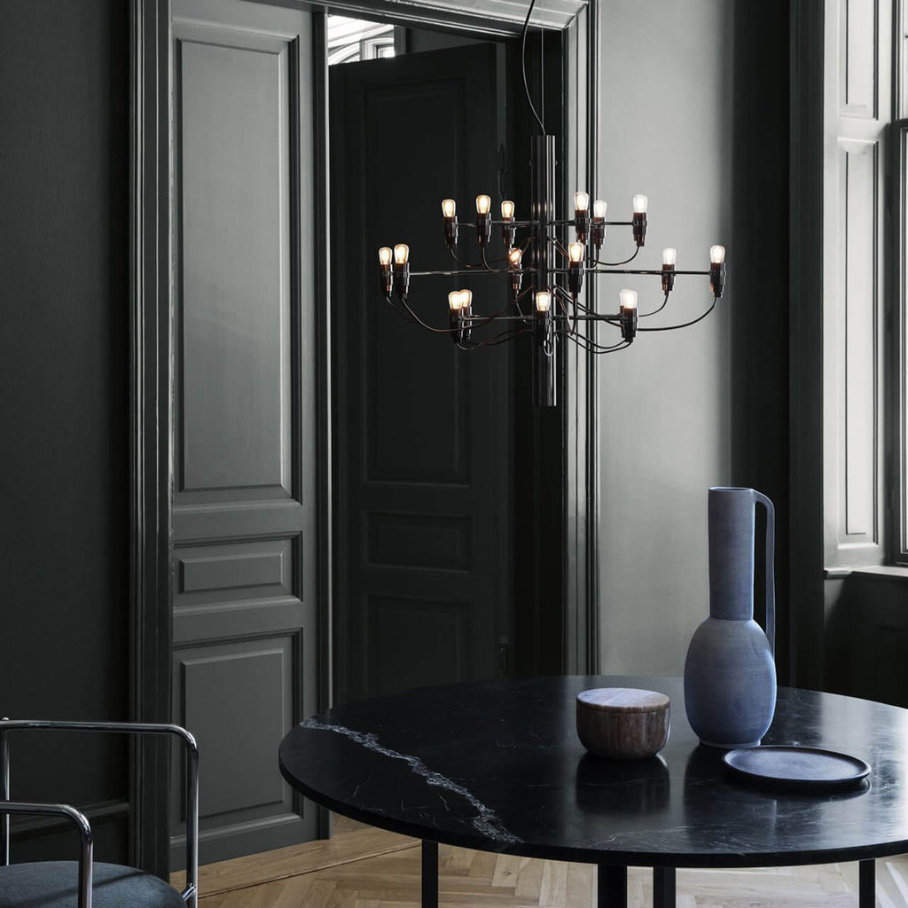 Warm bulbs light this Clérachic chandelier in front of dark panelled doors, above a black marble table and a blue vase.