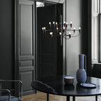 Warm bulbs light this Clérachic chandelier in front of dark panelled doors, above a black marble table and a blue vase.