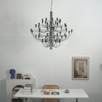 This Clérachic chandelier hangs against a white wall above a desk with books, a blue vase and a framed print.
