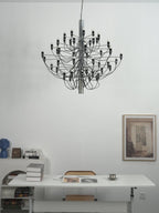 A Clérachic chandelier with slim arms hangs over a white desk, with a woven chair, books and a framed print behind.