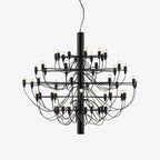 A Clérachic tiered chandelier in matt black, with slim arms and exposed bulbs around a central stem, on a plain white backdrop.