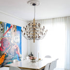 A gold-stemmed Clérachic chandelier hangs from a plaster ceiling rose over a white dining table, with a colourful mural at the left.