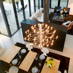 Seen from above, this Clérachic chandelier glows with exposed bulbs over a pale wood dining table set with plates and a vase of yellow flowers.