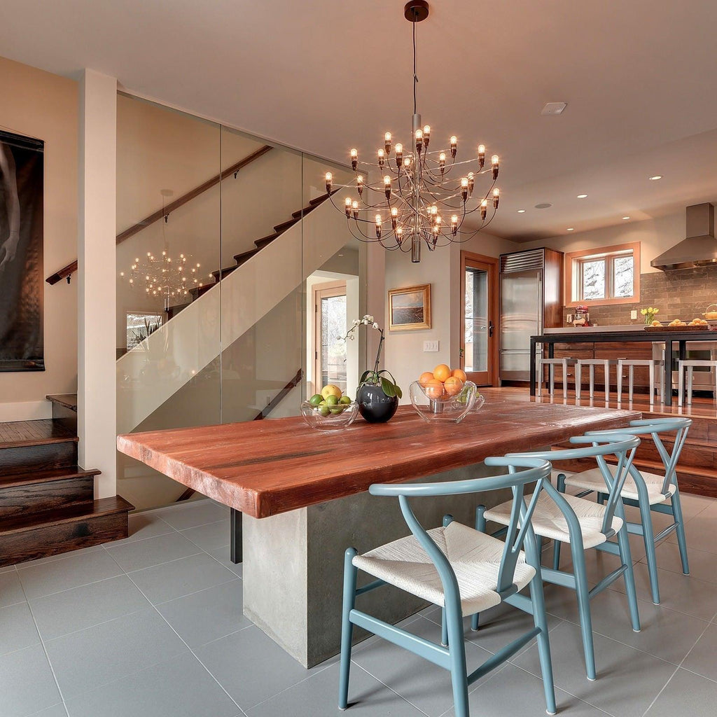Hung above a red wooden dining table with pale blue chairs, this Clérachic chandelier lights an open kitchen with a glass staircase.