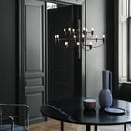 A Clérachic chandelier hangs near dark panelled doors, above a black marble table with a tall blue vase and a bowl.