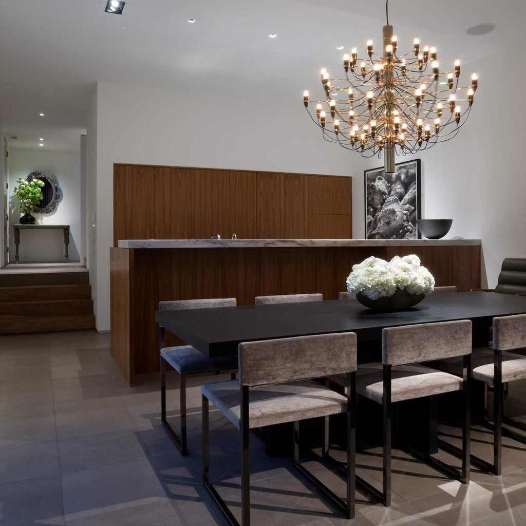 Warm bulbs light this gold-toned Clérachic chandelier over a dark dining table in a room with a walnut wall and a white flower bowl.