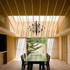 A matt black Clérachic chandelier hangs under a timber-slatted ceiling in a calm room, looking out to a garden.