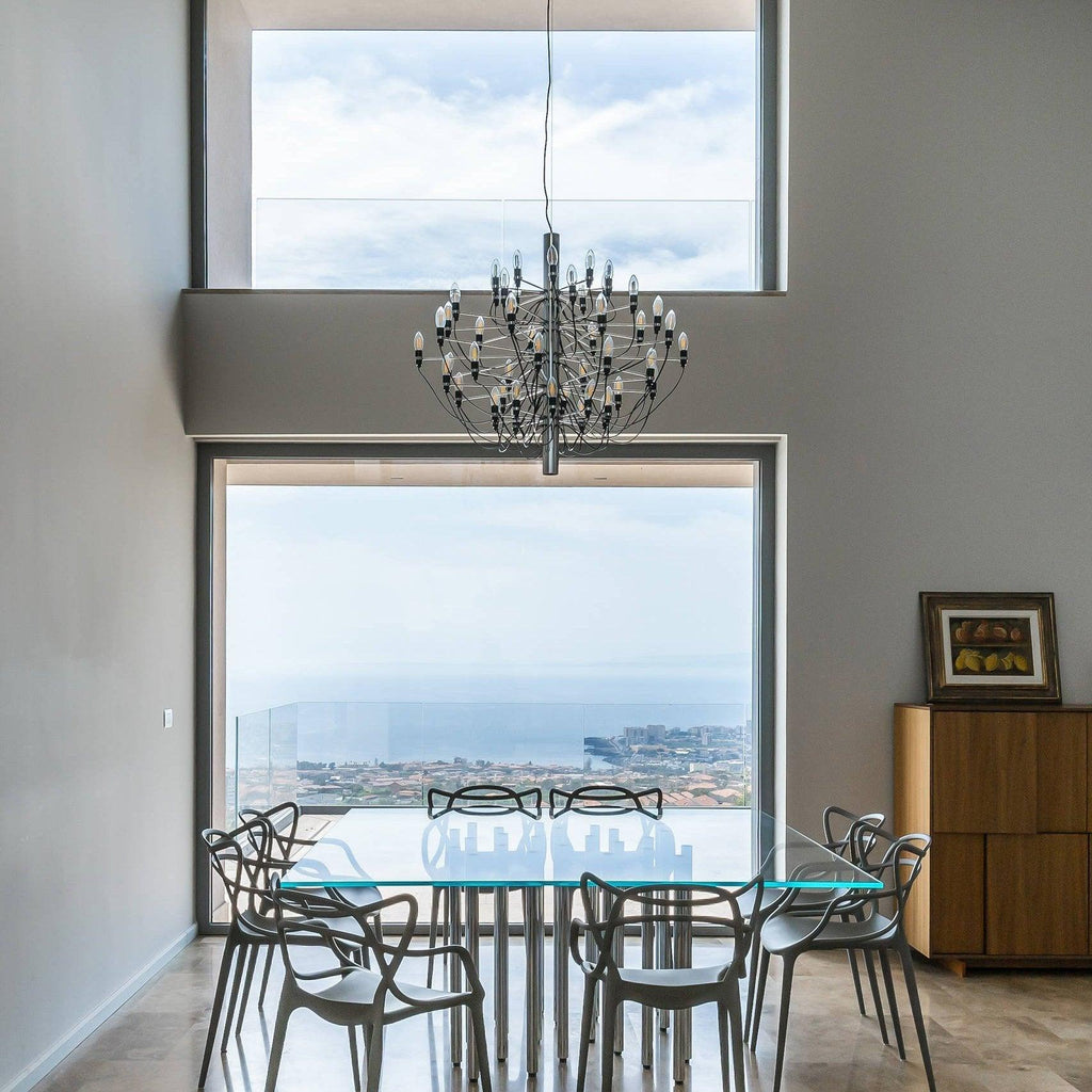 In a tall room with large picture windows, this Clérachic chandelier hangs above a glass dining table with sea views behind.