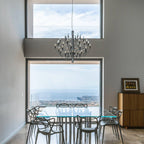 In a tall room with large picture windows, this Clérachic chandelier hangs above a glass dining table with sea views behind.