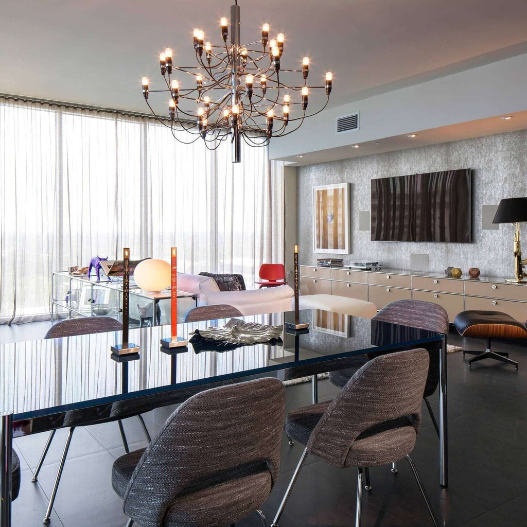 Warm bulbs light this Clérachic chandelier above a glossy dining table, with sheer curtains and a long sideboard behind.
