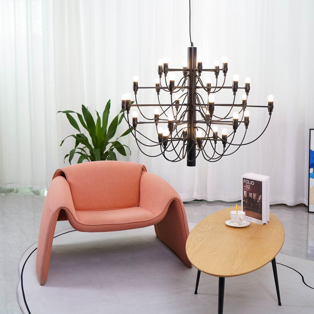 Seen close up, this matt black Clérachic chandelier hangs above a coral armchair and an oval table with a cup and book.