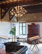 Seen from a wider angle, this Clérachic chandelier hangs in a timber-beamed room with leather sofas and wooden easels.