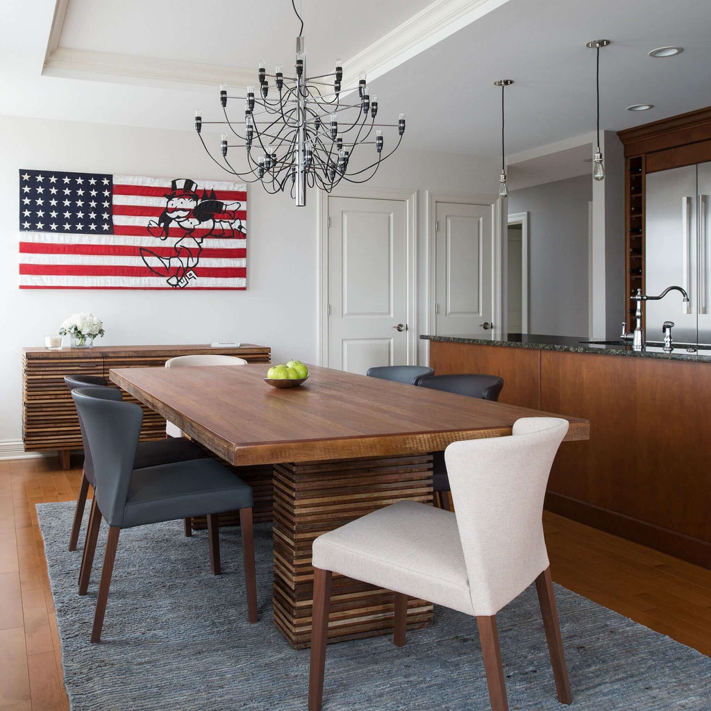 A Clérachic chandelier with a chrome stem hangs over a wooden table with grey and cream chairs in a kitchen-diner.