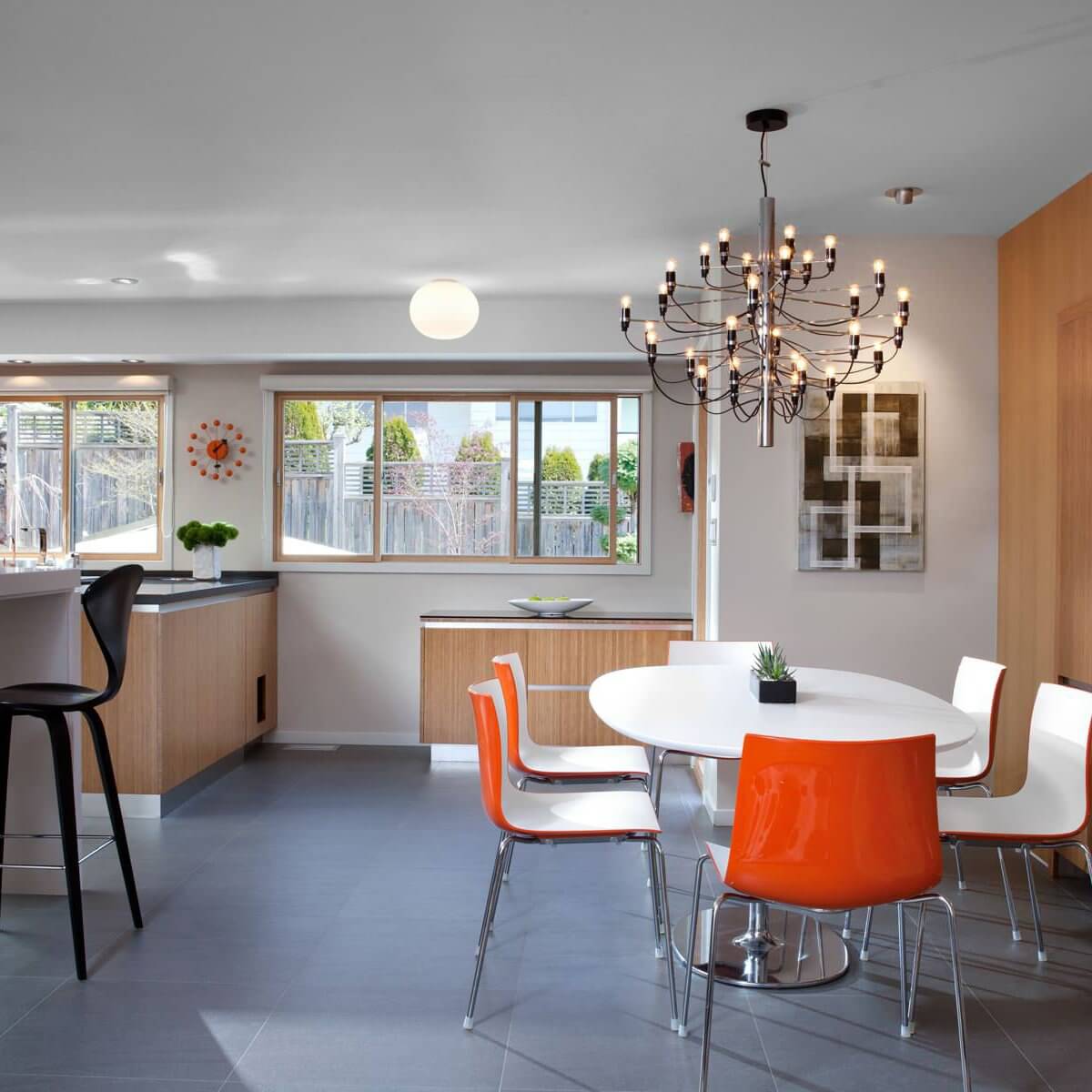 This Clérachic chandelier lights a bright kitchen with an oval white table, orange chairs and a wooden cabinet wall.