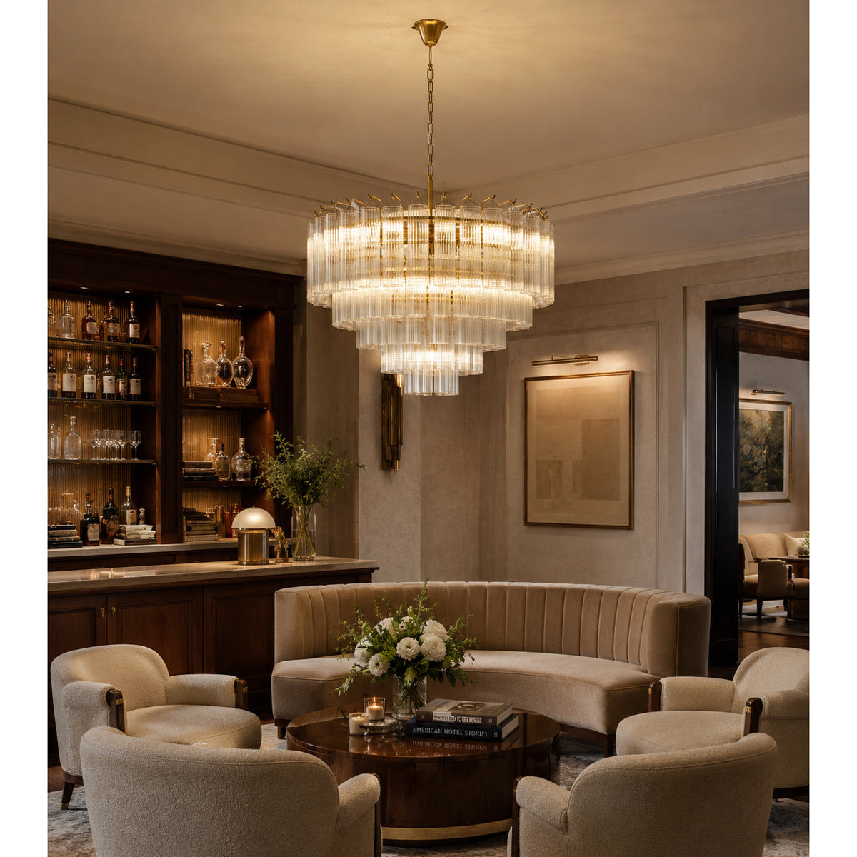 Clérachic glass-rod chandelier glowing above a curved sofa and low table, in a lounge with a lit wooden drinks cabinet.