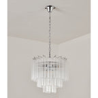 Switched-off Clérachic chandelier with a chrome canopy and chain and four tiers of clear fluted glass, in a pale corner.