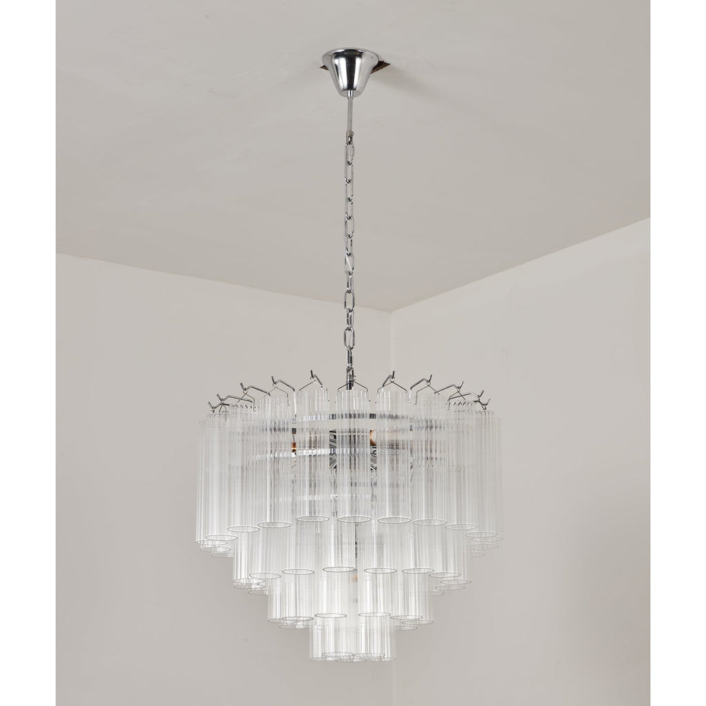 Unlit tiered glass chandelier from Clérachic on a chrome chain, the clear rods catching soft light in a plain room.