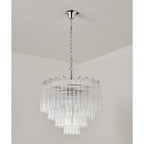 Unlit tiered glass chandelier from Clérachic on a chrome chain, the clear rods catching soft light in a plain room.