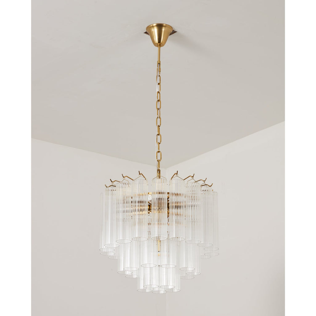 A smaller unlit Clérachic chandelier with clear glass rods and a gold-toned chain and canopy, in a pale room corner.