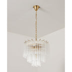 A smaller unlit Clérachic chandelier with clear glass rods and a gold-toned chain and canopy, in a pale room corner.