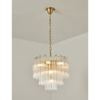 Warmly lit Clérachic chandelier with a gold-toned frame, its tiers of clear fluted glass glowing against a cream wall.