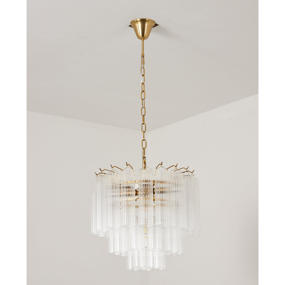 Unlit Clérachic chandelier with clear ribbed glass rods around a gold-toned frame, hanging from a short chain.