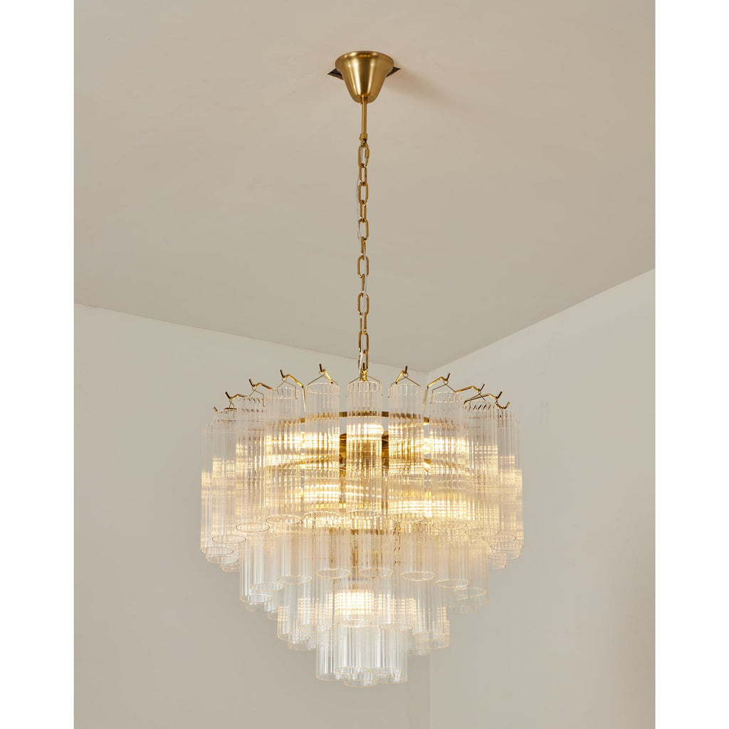 Lit mid-size Clérachic glass chandelier with a gold-toned chain, the light warm between the stepped layers of rods.