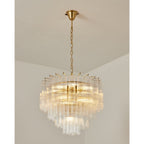 Lit mid-size Clérachic glass chandelier with a gold-toned chain, the light warm between the stepped layers of rods.