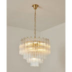 Clérachic tiered glass chandelier glowing evenly, its gold-toned chain rising to a small ceiling cup in a white corner.
