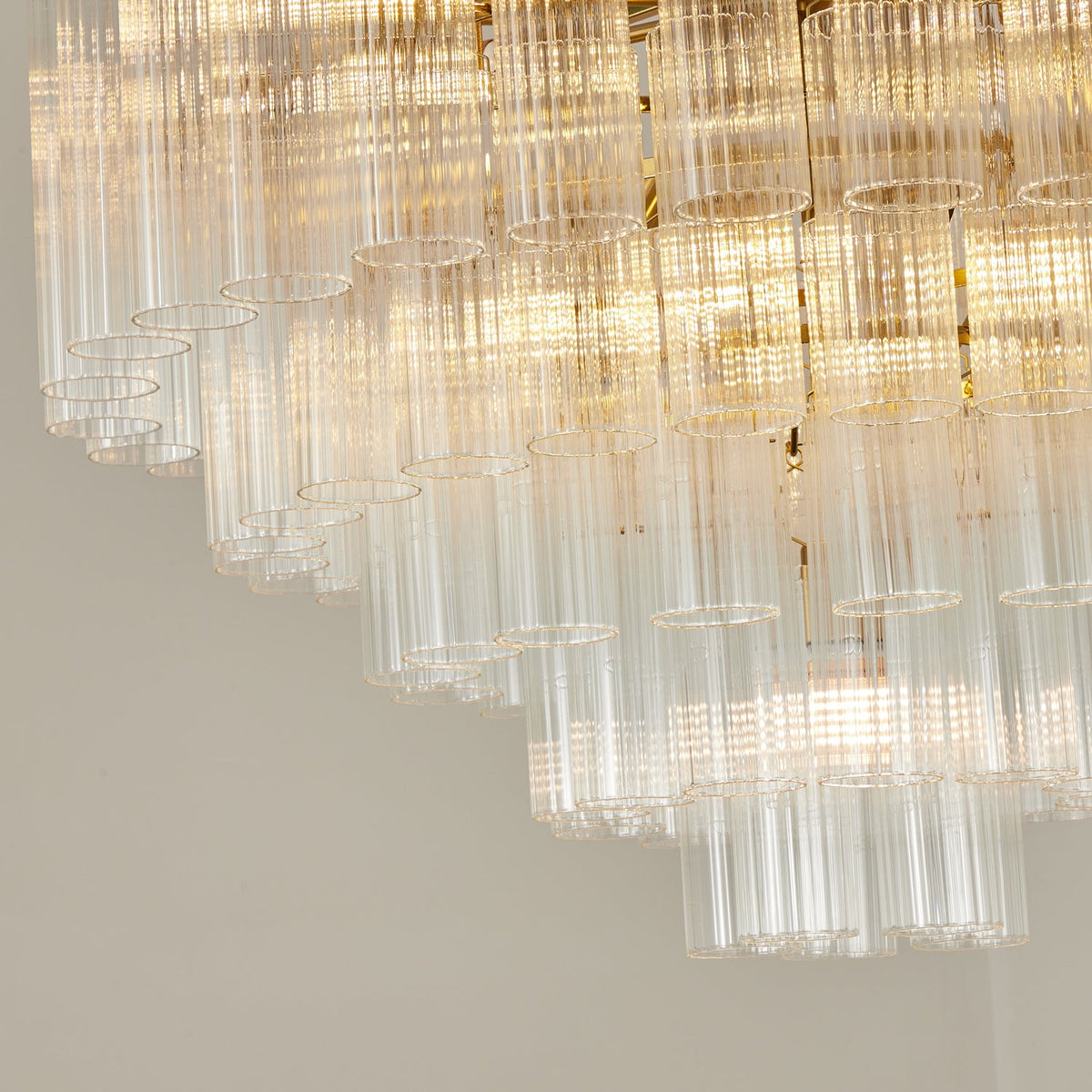 Close view of the lower tiers of this Clérachic chandelier, lit, with open-ended fluted glass rods in stepped rows.