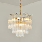 A Clérachic tiered glass chandelier shining against a pale wall, its gold-toned hooks visible around the upper rim.