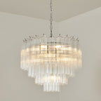Chrome-fitted Clérachic glass chandelier glowing warm in a room corner, with the rods stepped in graduated lengths.