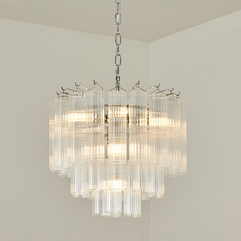Lit Clérachic chandelier on a chrome chain with several tiers of clear glass, set against a light cream wall.