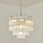 Lit Clérachic chandelier on a chrome chain with several tiers of clear glass, set against a light cream wall.
