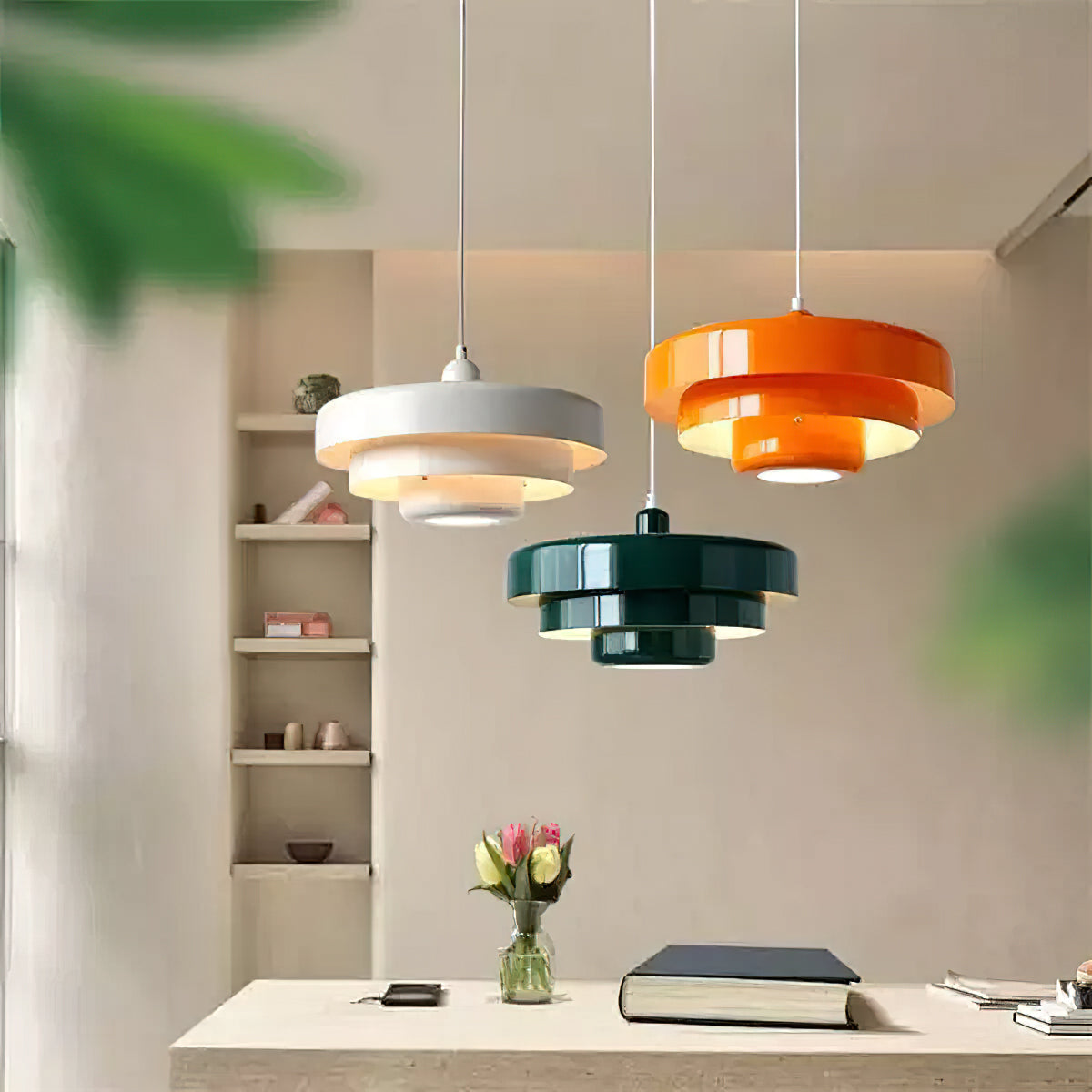 Three Clérachic tiered pendants in white, orange and dark green at different heights in a pale room with shelves and a bunch of tulips.