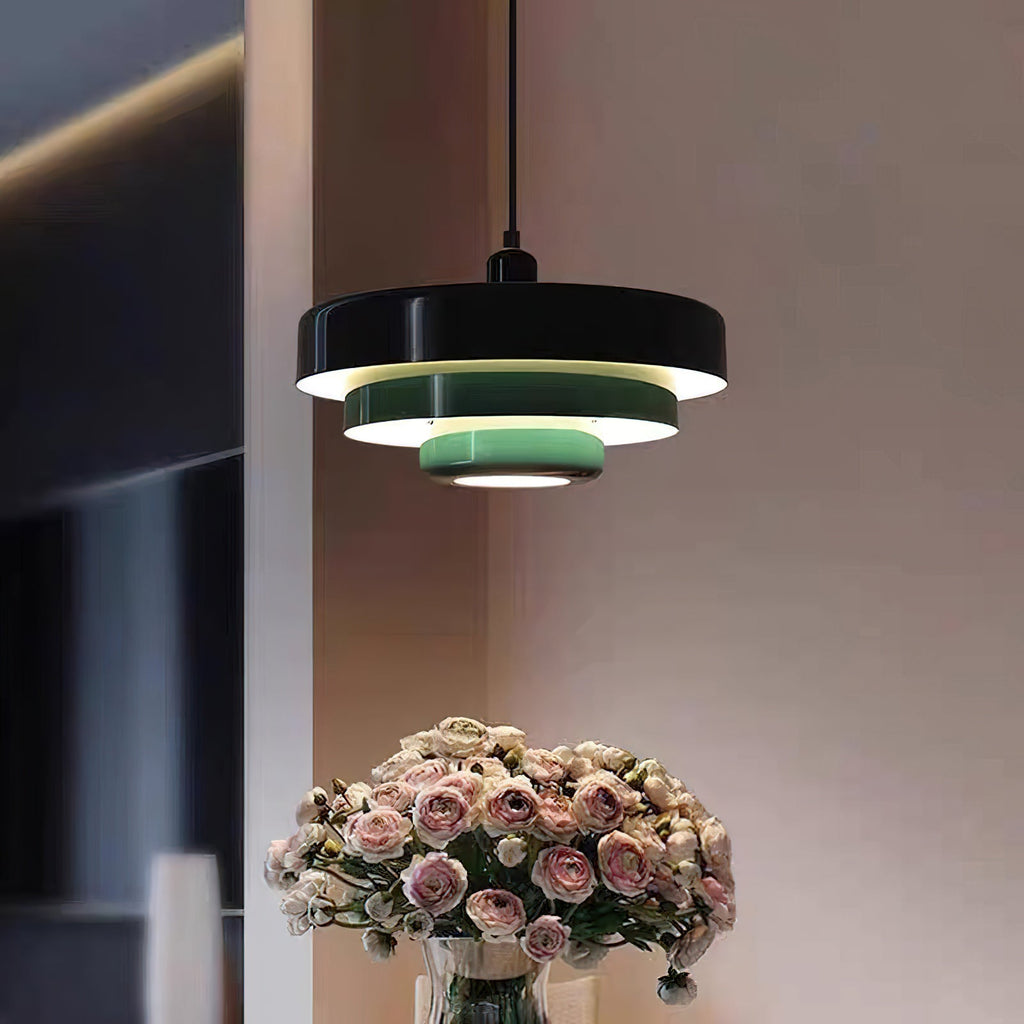 A Clérachic tiered pendant with a black top tier and pale green lower tiers beside a vase of pink roses, on a mauve wall.