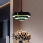 A Clérachic tiered pendant with a black top tier and pale green lower tiers beside a vase of pink roses, on a mauve wall.