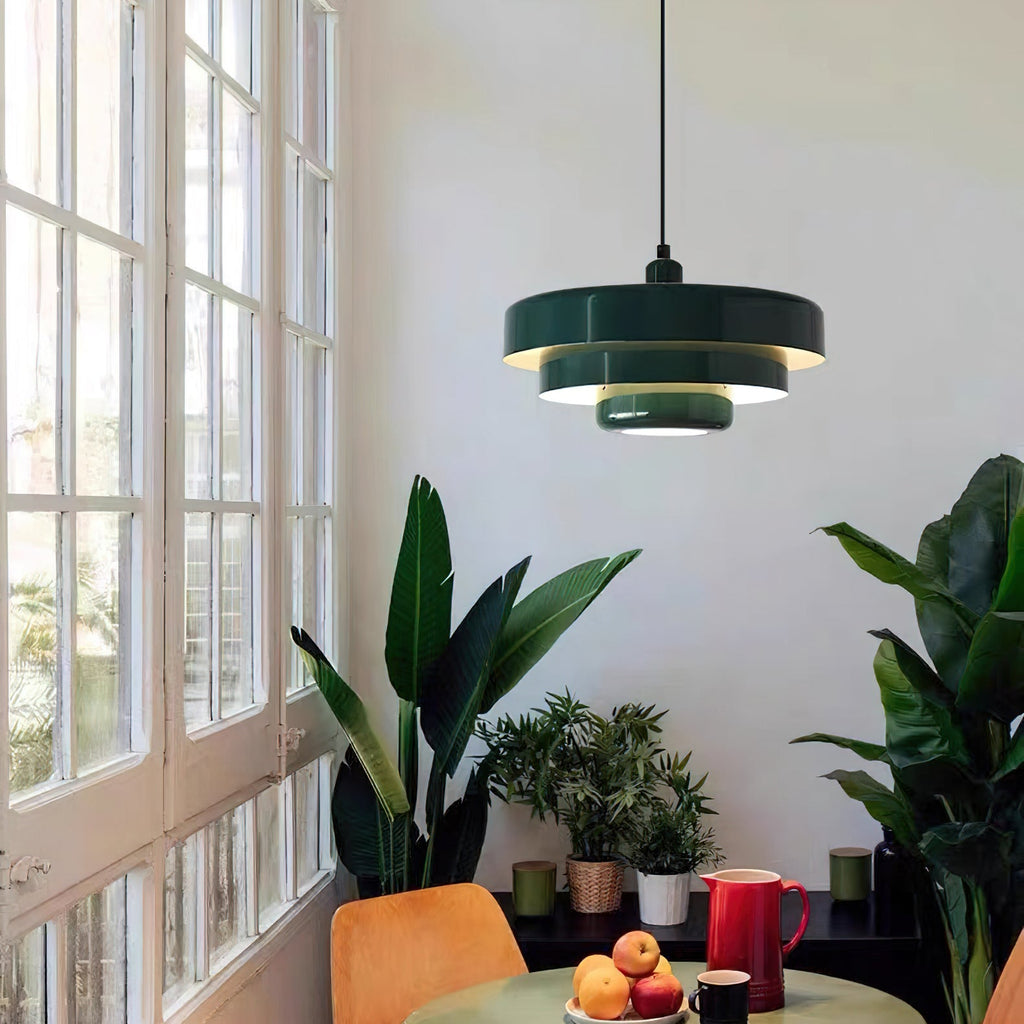 A dark green Clérachic tiered pendant in a bright room with tall white-framed windows, above a small table with a red jug and fruit.