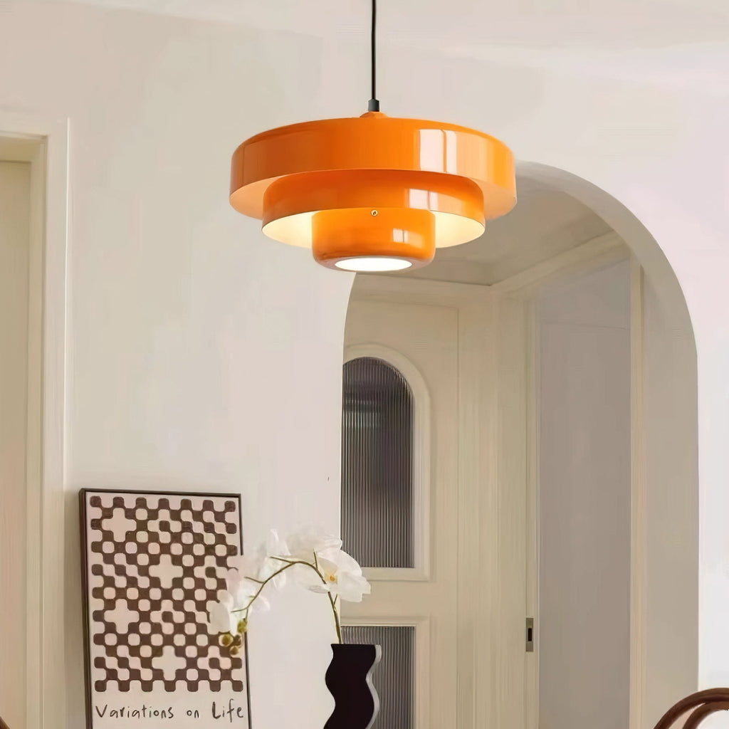 An orange Clérachic tiered pendant on a black cord by an arched doorway, with a checked print and a white orchid below.