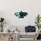 A dark green Clérachic tiered pendant hanging above a low table and a cream sofa with a knotted grey cushion and tall plants.