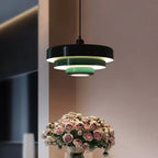 Close view of a Clérachic tiered pendant with a black top tier and pale green lower tiers, lit above a vase of pink roses.