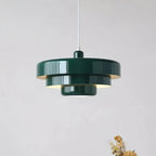 Close view of a dark green Clérachic tiered pendant against a plain pale wall, with its three tiers and lit underside visible.