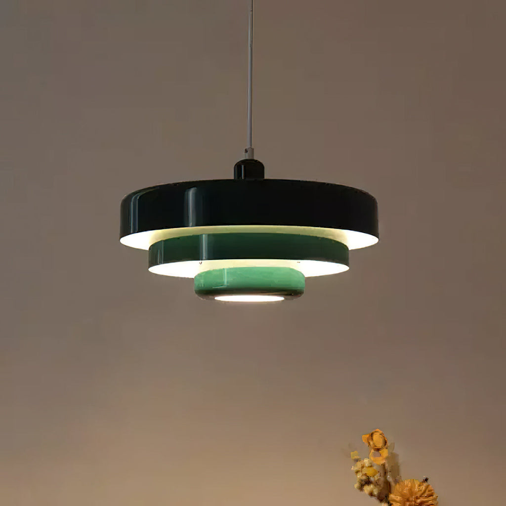A Clérachic tiered pendant with a black top tier and pale green lower tiers, lit against a warm brown wall.