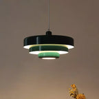 A Clérachic tiered pendant with a black top tier and pale green lower tiers, lit against a warm brown wall.