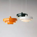 Three Clérachic tiered pendants in orange, dark green and white at staggered heights on white cords against a pale grey wall.