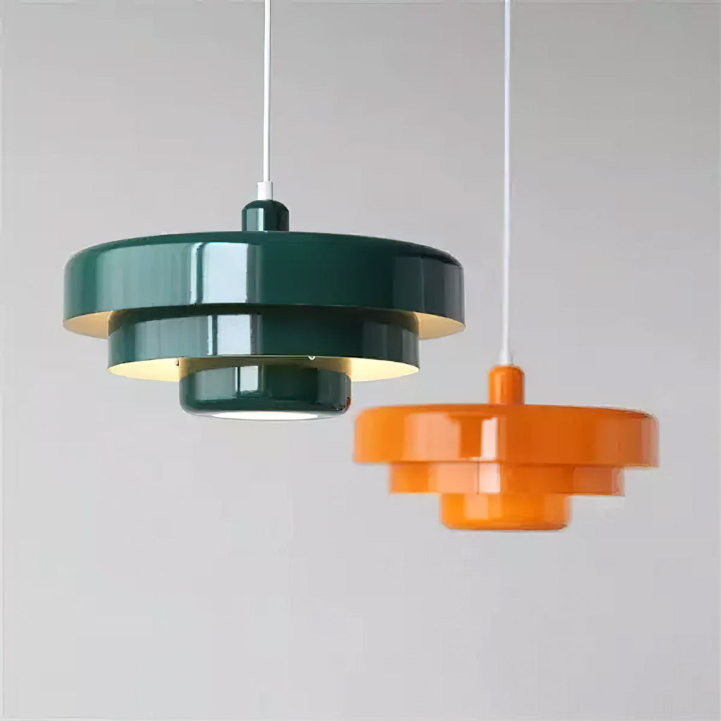 A dark green Clérachic tiered pendant hanging beside a smaller orange one at a different height, against a pale grey wall.