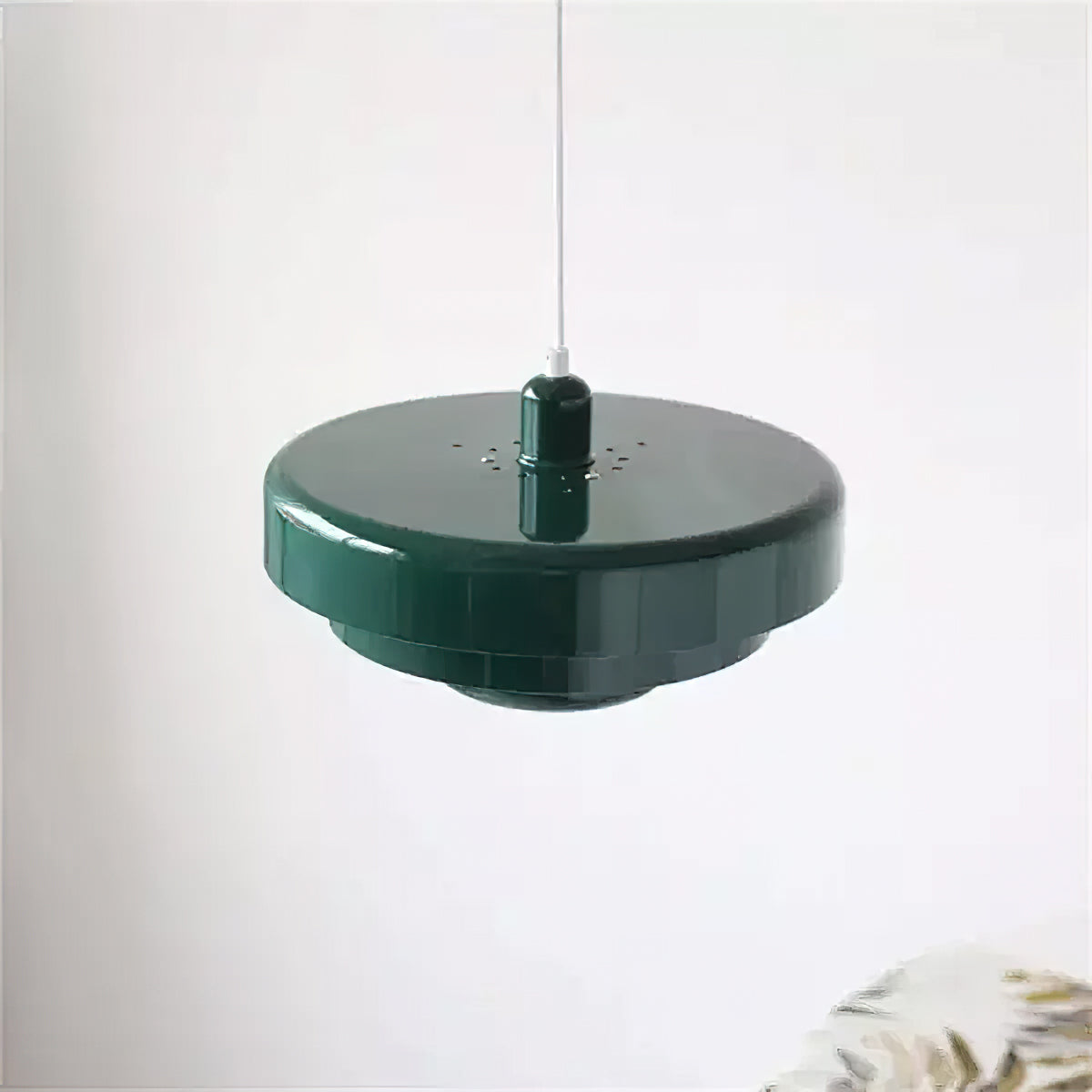 Top-down angle of a dark green Clérachic tiered pendant against a pale wall, showing the smooth top disc and the small vent holes.