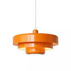 An orange Clérachic tiered pendant on a white cord against a white backdrop, with glossy tiers and a lit underside.