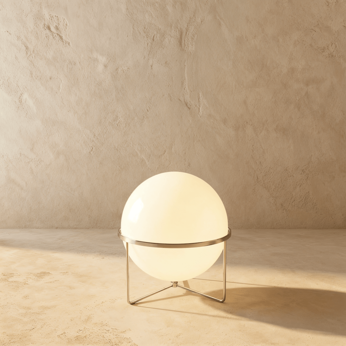 Clérachic single-globe sphere lamp in silver, glowing warm on its wire tripod against the same plaster backdrop.