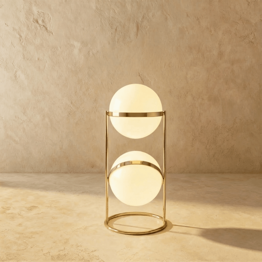 Clérachic two-globe sphere lamp in polished brass, the short column lit against a plaster studio wall.